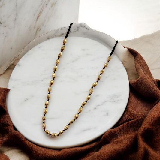 Hemali Suvarna Thread Ganthan Necklace - gold oval bead black thread traditional Maharashtrian necklace displayed on marble plate , maharashtrian jewellery under 500