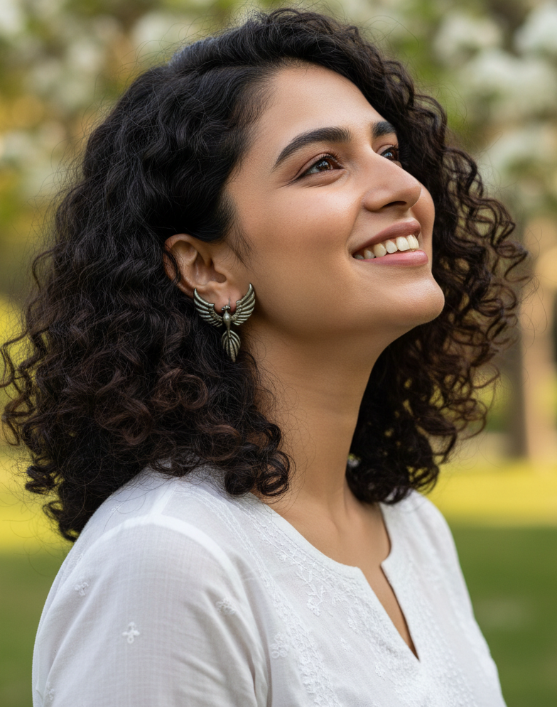 Silver bird oxidised studs being worn by a Woman with curly hair smiling outdoors wearing a white kurta