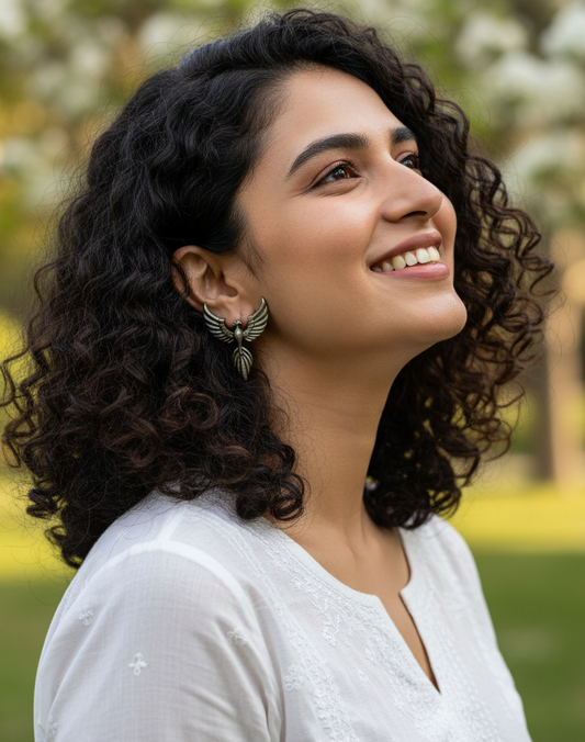 Silver bird oxidised studs being worn by a Woman with curly hair smiling outdoors wearing a white kurta