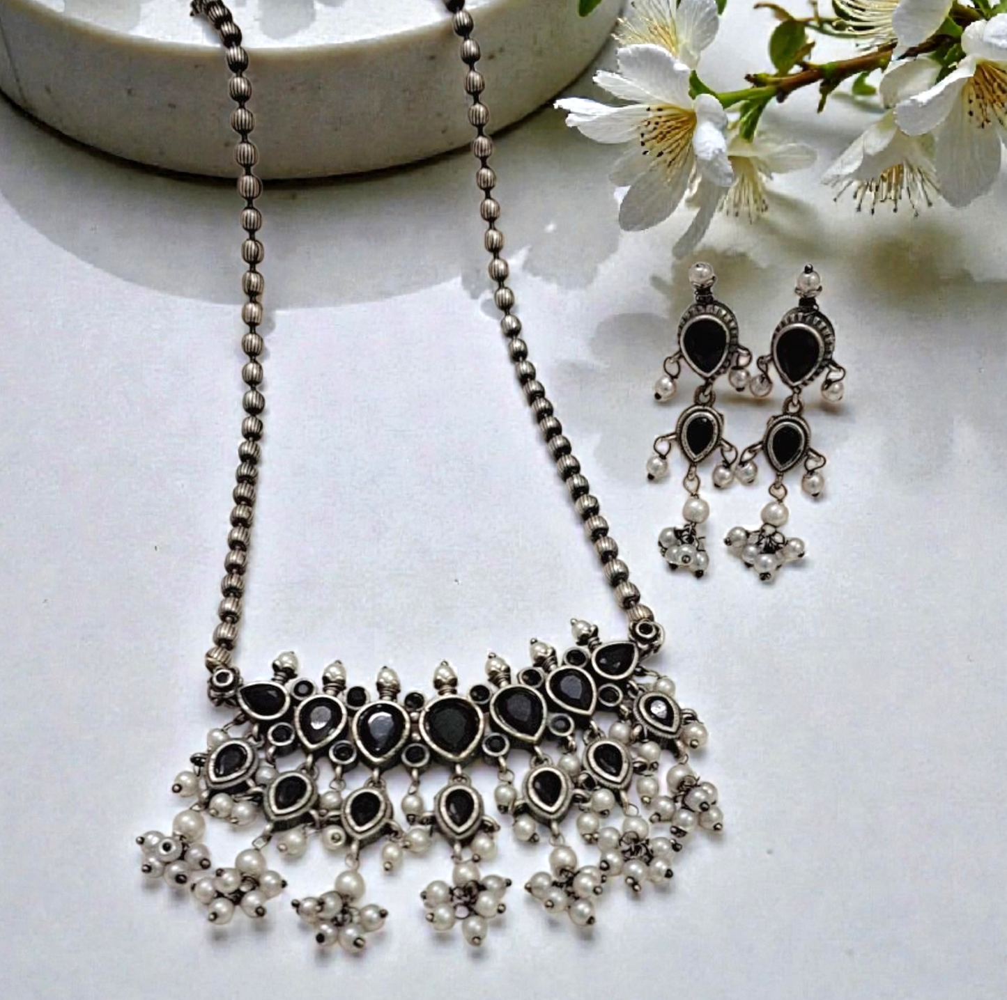 This oxidised black stone necklace set features antique silver finish detailing with pearl drops and matching earrings. Ideal ethnic statement jewellery for festive wear, weddings and traditional styling.