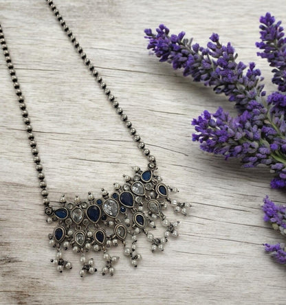 This oxidised blue and white stone necklace set features antique silver finish detailing with pearl drops and matching earrings. Ideal vintage ethnic statement jewellery for festive wear, weddings and traditional styling.