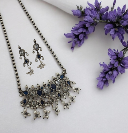 This oxidised blue and white stone necklace set features antique silver finish detailing with pearl drops and matching earrings. Ideal vintage ethnic statement jewellery for festive wear, weddings and traditional styling.