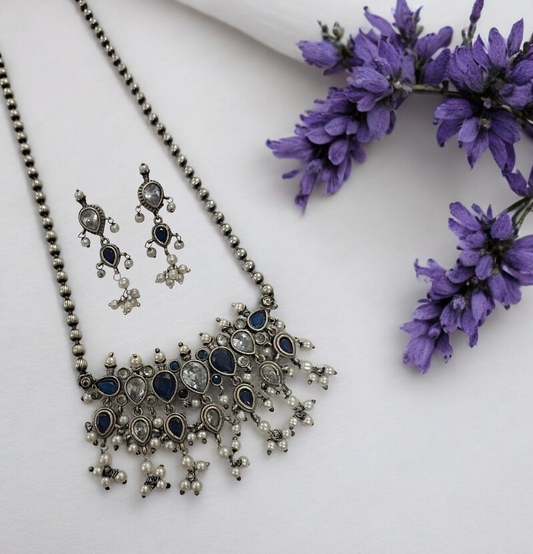 This oxidised blue and white stone necklace set features antique silver finish detailing with pearl drops and matching earrings. Ideal vintage ethnic statement jewellery for festive wear, weddings and traditional styling.