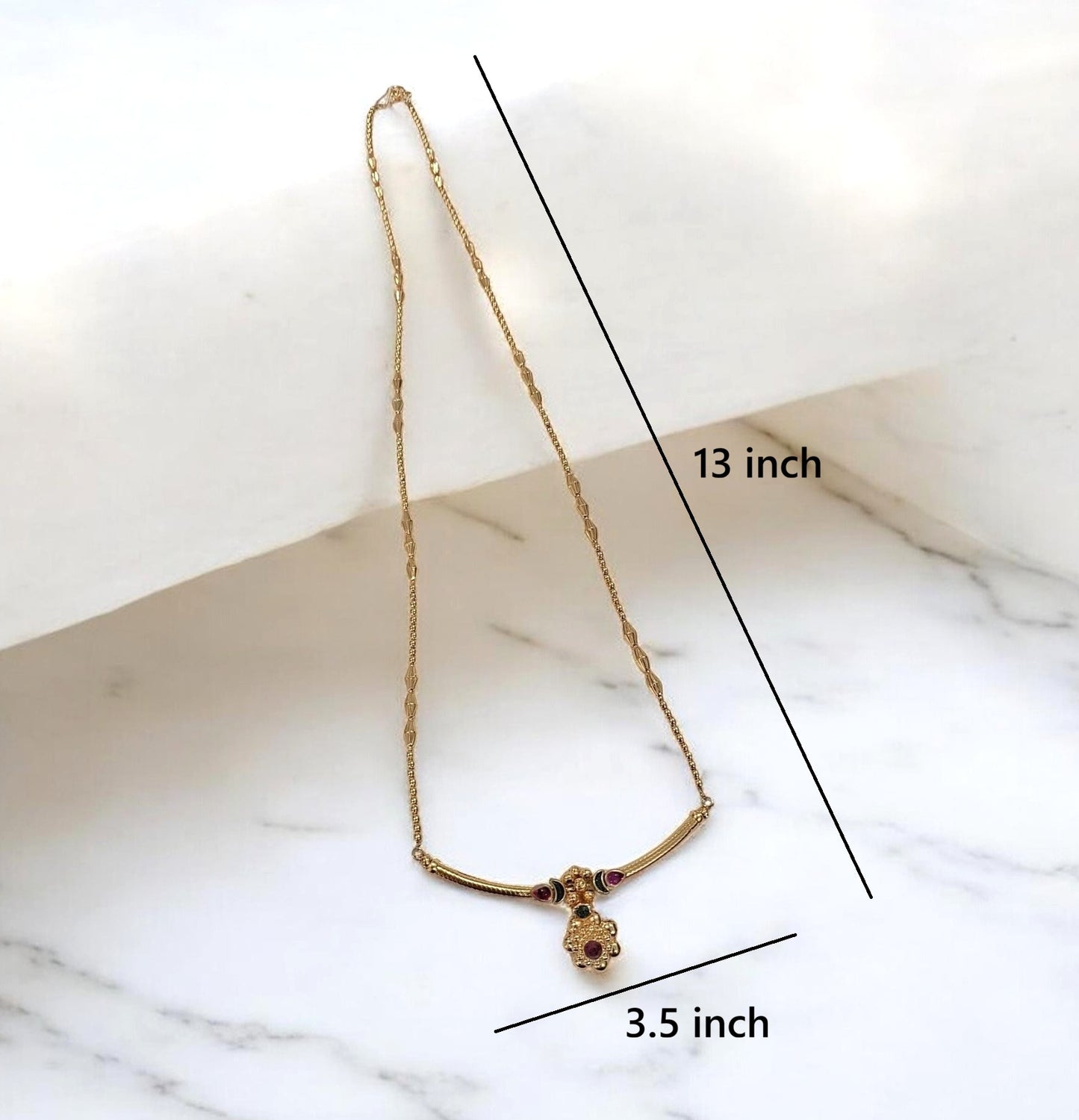 Gold necklace with a small pendant displayed on a white marble surface, with black measurement lines and text indicating 13 inch length and 3.5 inch width.