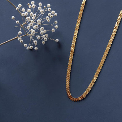 Uparna gold plated leaf chain long necklace laid flat on a navy blue background with dried white wildflowers
