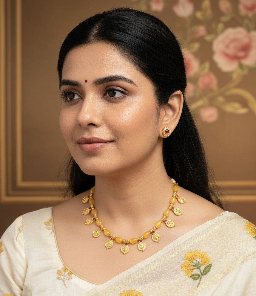 Woman wearing Vaibhavi Yellow Beaded Lakshmi coin necklace and matching stud earrings, paired with floral cream saree