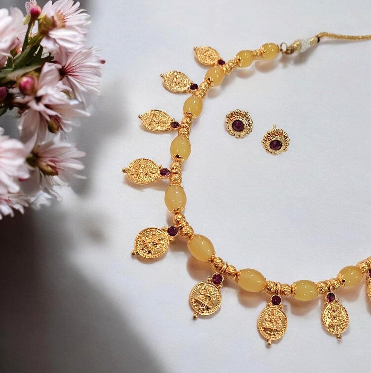 Vaibhavi yellow beaded Lakshmi coin necklace and gold studs earrings, close-up flat lay view